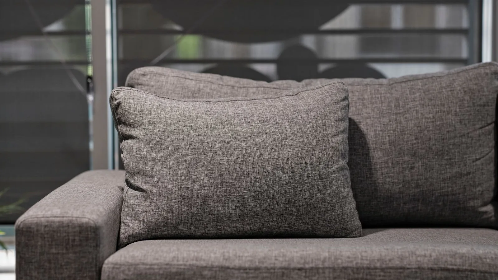 Close-up of a grey woven fabric sofa seat, arm and cushion beside a window