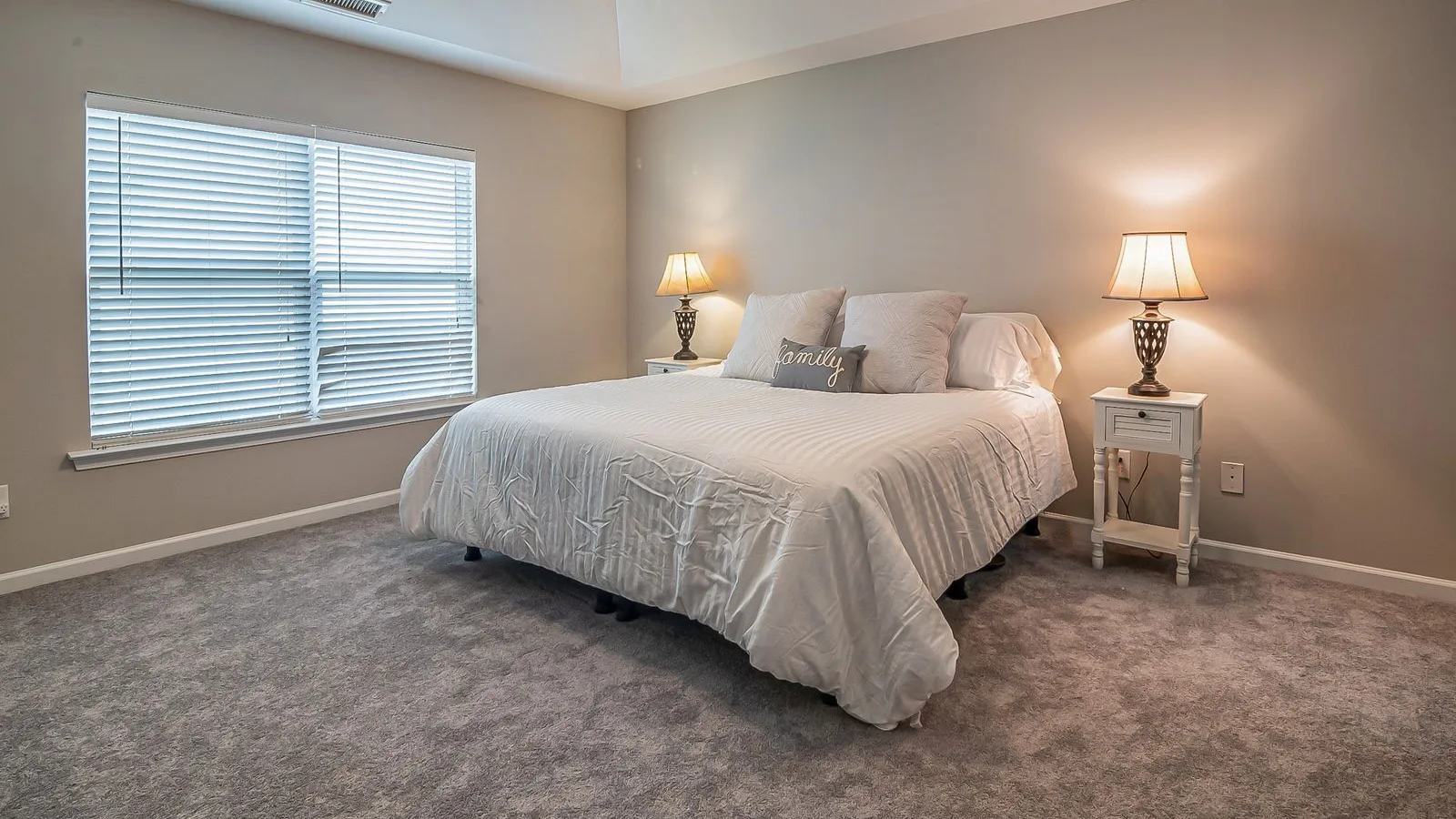A carpeted bedroom with a made bed and two bedside lamps