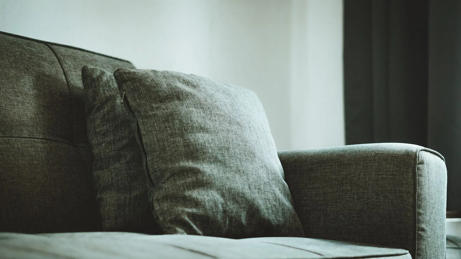 Grey-green woven fabric couch with two scatter cushions against the arm