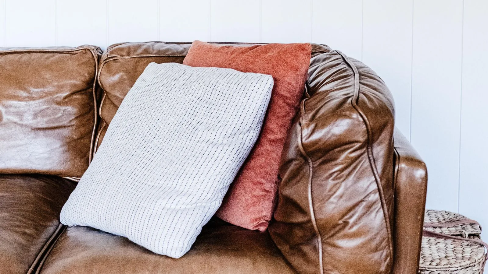 Brown leather sofa with cushions against a white panelled wall, showing the sheen and seams of finished leather