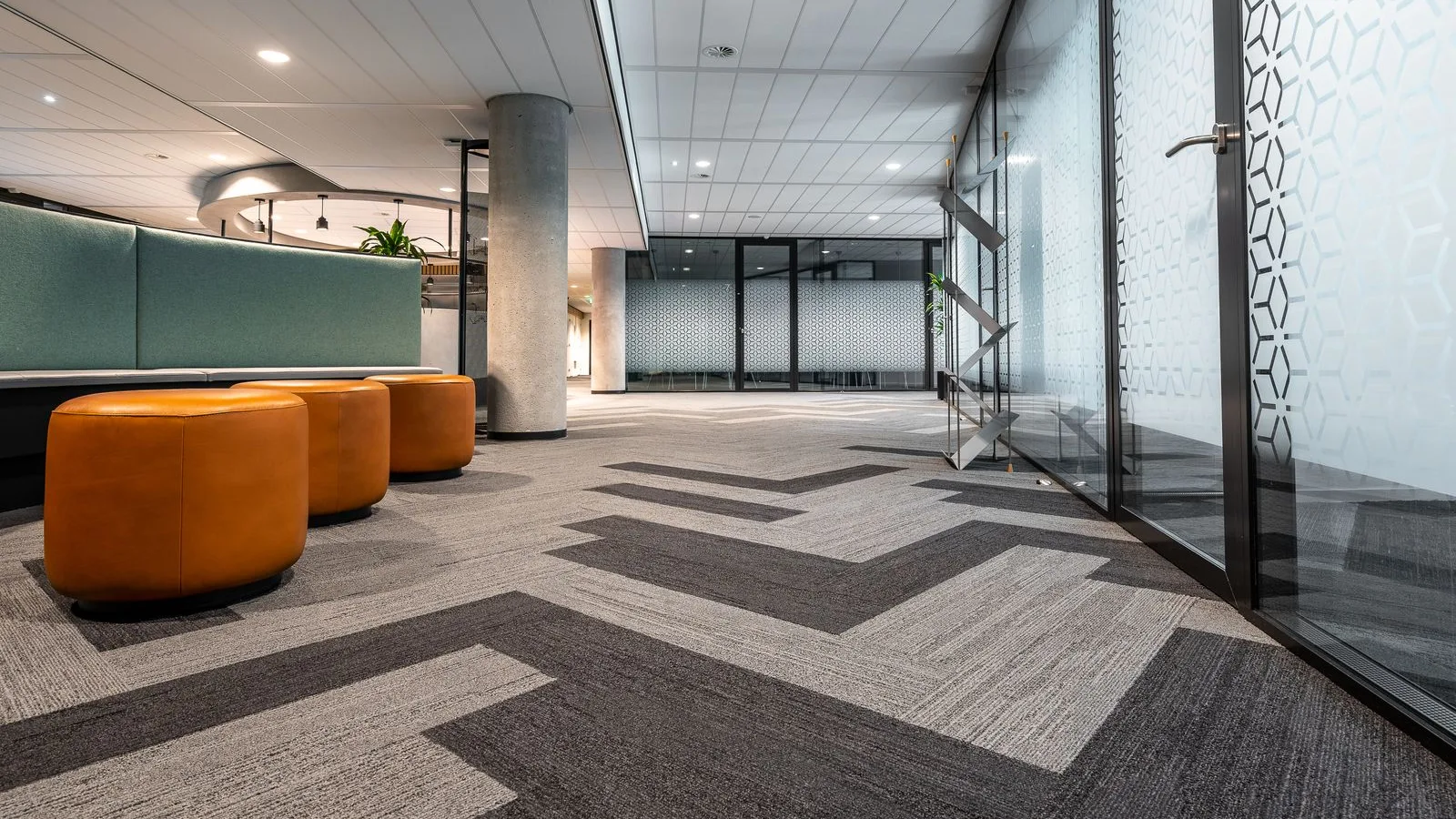 Office corridor floored with grey and charcoal carpet tile planks laid in a herringbone pattern