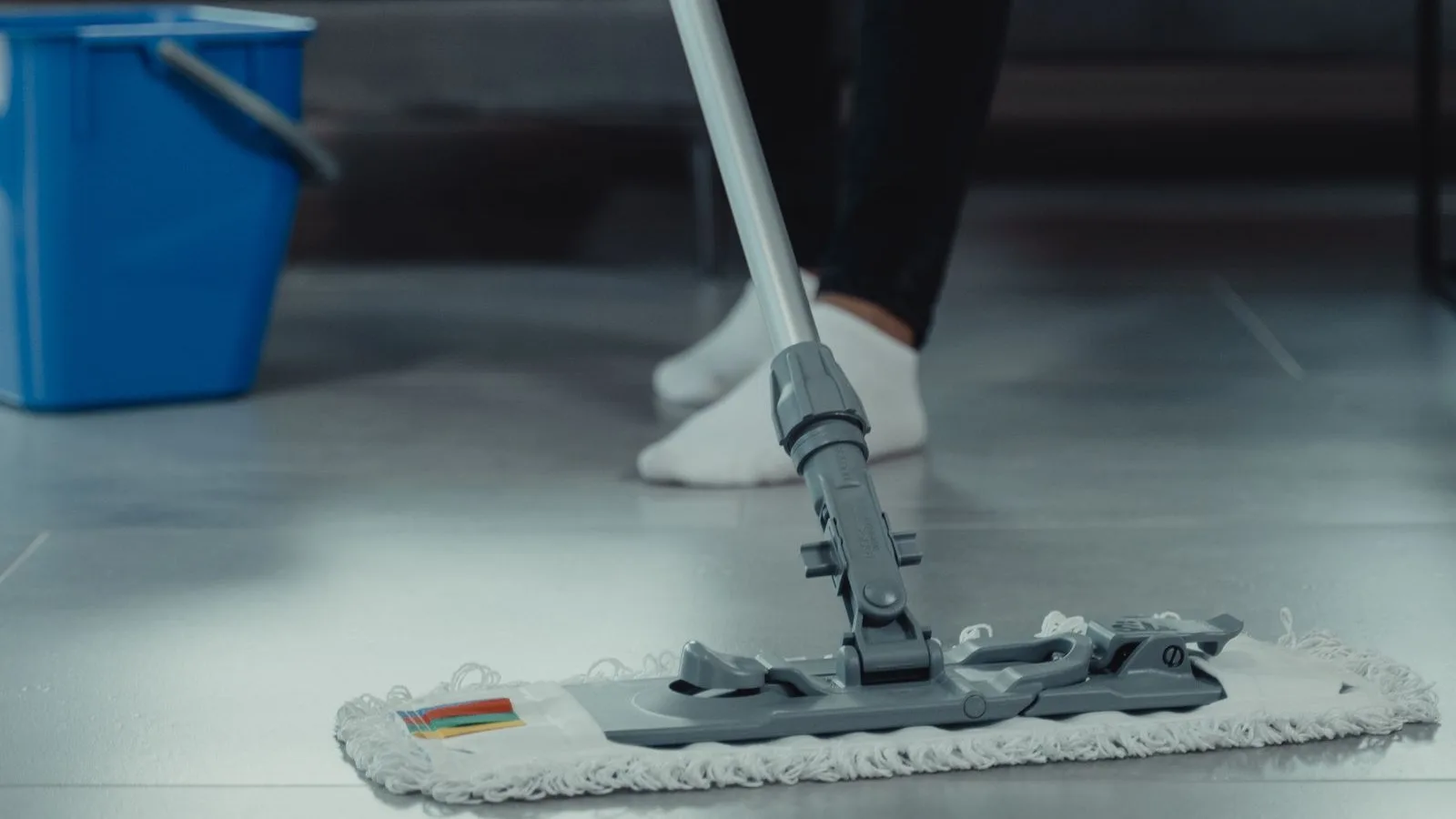 Flat microfibre mop on grey floor tiles with a blue bucket in the background