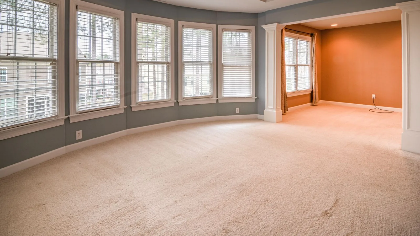 Cream wall-to-wall carpet across an empty living room, the pile lying flat where the room is walked through