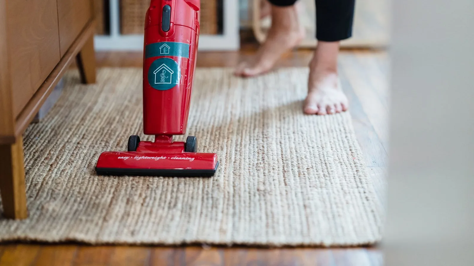 A household upright vacuum being pushed across a woven rug in a sunlit living room