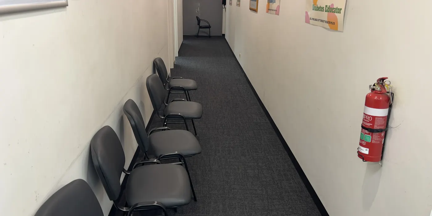 A corridor at the same Tarneit clinic after cleaning, the carpet even from wall to wall past the row of seating.